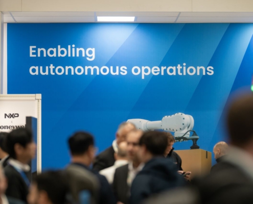Blaues NXP-Messebanner mit dem Schriftzug „Enabling autonomous operations“ hinter Messebesuchern