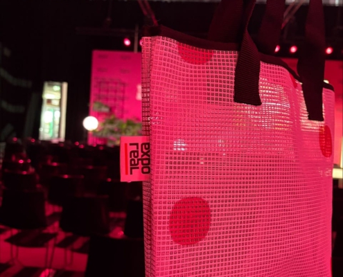 Einkaufstasche aus einem EXPO REAL-Mesh-Banner mit großen Punkten und schwarzen Henkeln in einer pink beleuchteten Veranstaltungshalle